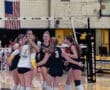 High school volleyball team celebrating a point, showcasing teamwork and enthusiasm in a gymnasium setting.