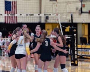 High school volleyball team celebrating a point, showcasing teamwork and enthusiasm in a gymnasium setting.