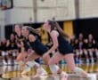 Three female volleyball players focused and ready during a game, with teammates in the background, showcasing athleticism.