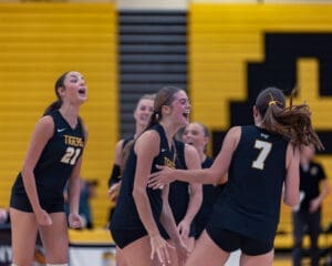 Girls' volleyball team celebrating a point in a spirited game, showcasing teamwork and enthusiasm on the court.