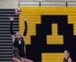Volleyball player sets the ball high during a match, teammates positioned and ready, school colors in the background.