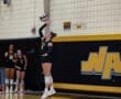 Female volleyball player from the Tigers team serves the ball during a match, with teammates in the background.