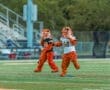 Two playful tiger mascots in team jerseys entertain the crowd on a sports field during an event.