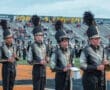High school marching band members in uniforms holding clarinets during a performance on an outdoor field.
