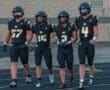 Four football players in black and gold uniforms walking together on the field, showcasing teamwork and camaraderie.