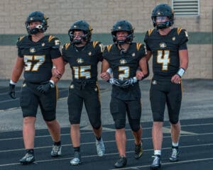Four football players in black and gold uniforms walking together on the field, showcasing teamwork and camaraderie.