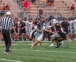 Quarterback evades a tackle during a high school football game, with players and spectators in the background.