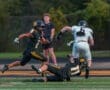 High school football players in action: a black team tackles a player in white on the field during a competitive game.