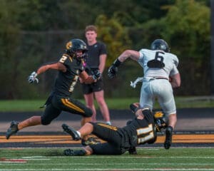 High school football players in action: a black team tackles a player in white on the field during a competitive game.