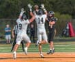 Football players in action, with two defenders attempting to intercept a pass from the quarterback on the field.