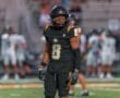 Football player in a black jersey and helmet, poised on the field during a game, showcasing determination and focus.