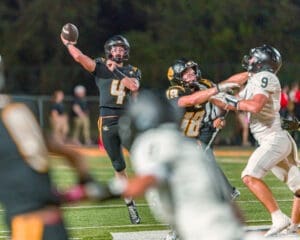 Quarterback throws a pass under pressure during a night football game, showcasing intense action on the field.