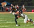 High school football players competing, one running with the ball, while the other attempts to tackle him on the field.