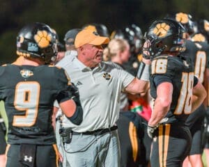 Football coach guiding players during a game, highlighting teamwork and strategy on the field.