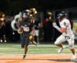 A player in a black football uniform dodges a white opponent while running with the ball on a night stadium field.