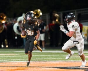 A player in a black football uniform dodges a white opponent while running with the ball on a night stadium field.
