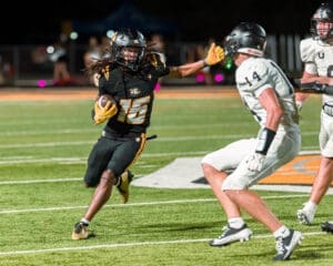 Football player #16 dodges opponents on the field during a night game, showcasing athleticism and skill.