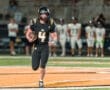 Quarterback #4 runs with the football during a high school football game under the stadium lights.
