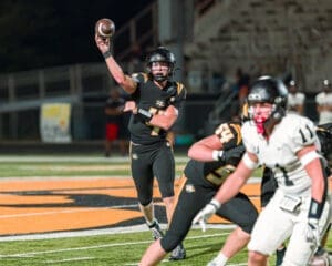 Quarterback throwing a football during a high school football game on a night filled with action.