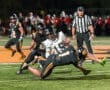A football player is tackled during a high school game, showcasing intense action on the sports field under bright lights.
