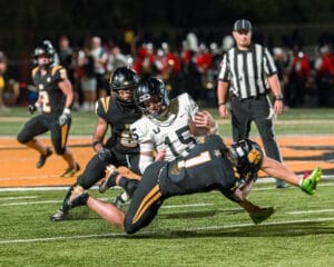 A football player is tackled during a high school game, showcasing intense action on the sports field under bright lights.