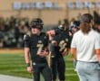 Two young football players in black uniforms discuss strategy on the sidelines of a night game at the Baierl Center.