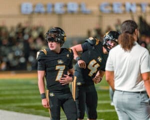 Two young football players in black uniforms discuss strategy on the sidelines of a night game at the Baierl Center.