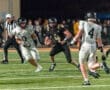 High school football player in black uniform evades a defender in white during a night game on a turf field.