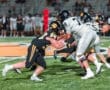 High school football players clash on the field, highlighting intense action during a night game under stadium lights.