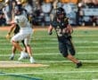 Player in black uniform dodges a defender in white during a football game under stadium lights. Action-packed moment.