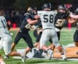 Two football players engage in a fierce block on the field under stadium lights during a competitive game.
