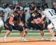 Two football players in black uniforms prepare for a play on the field during a night game, showcasing teamwork and strategy.