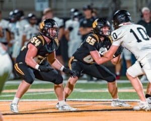 Two football players in black uniforms prepare for a play on the field during a night game, showcasing teamwork and strategy.