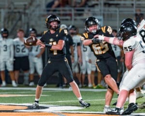 High school quarterback throws a pass under pressure during a night football game on the field.