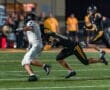 A football player in a white jersey is tackled from behind by an opponent in a black jersey during a night game.