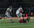 Football players in action during a night game, with one player being tackled on the field.