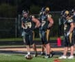 Football players in black uniforms strategizing on the field during a nighttime game. Teamwork and competition highlighted.