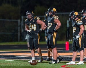 Football players in black uniforms strategizing on the field during a nighttime game. Teamwork and competition highlighted.