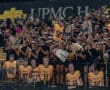 Excited football fans at a night game holding player cutouts, dressed in black and gold, showing school spirit.