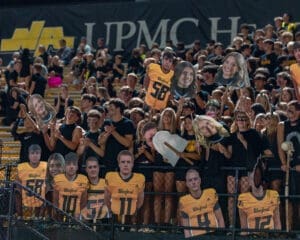 Excited football fans at a night game holding player cutouts, dressed in black and gold, showing school spirit.