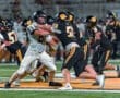 High school football players in action, showcasing a tackle during a night game on a well-lit field.