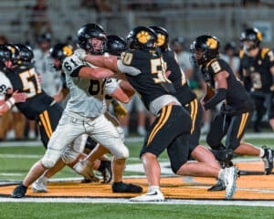 High school football players in action, showcasing a tackle during a night game on a well-lit field.