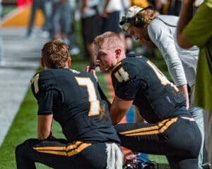 Two football players discuss strategies on the sidelines during a game, showcasing teamwork and focus in sports.