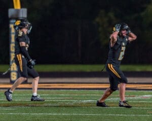 Two football players on the field, one celebrating and the other reacting, under bright stadium lights at night.