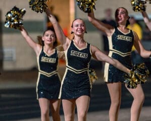 Cheerleaders in glittering uniforms performing at a night game, showcasing team spirit with vibrant pom-poms.