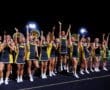 Cheerleaders in vibrant uniforms celebrating and performing under stadium lights at a spirited night event.