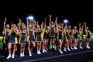 Cheerleaders in vibrant uniforms celebrating and performing under stadium lights at a spirited night event.