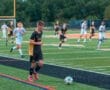 Youth soccer game in action, showing players sprinting on a vibrant turf field with a focus on a player dribbling the ball.