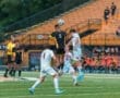 High school soccer match with players in action, one leaping to head the ball amid a vibrant crowd on the sidelines.