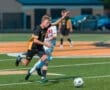 High school soccer players compete for the ball on a green turf field during an intense match.
